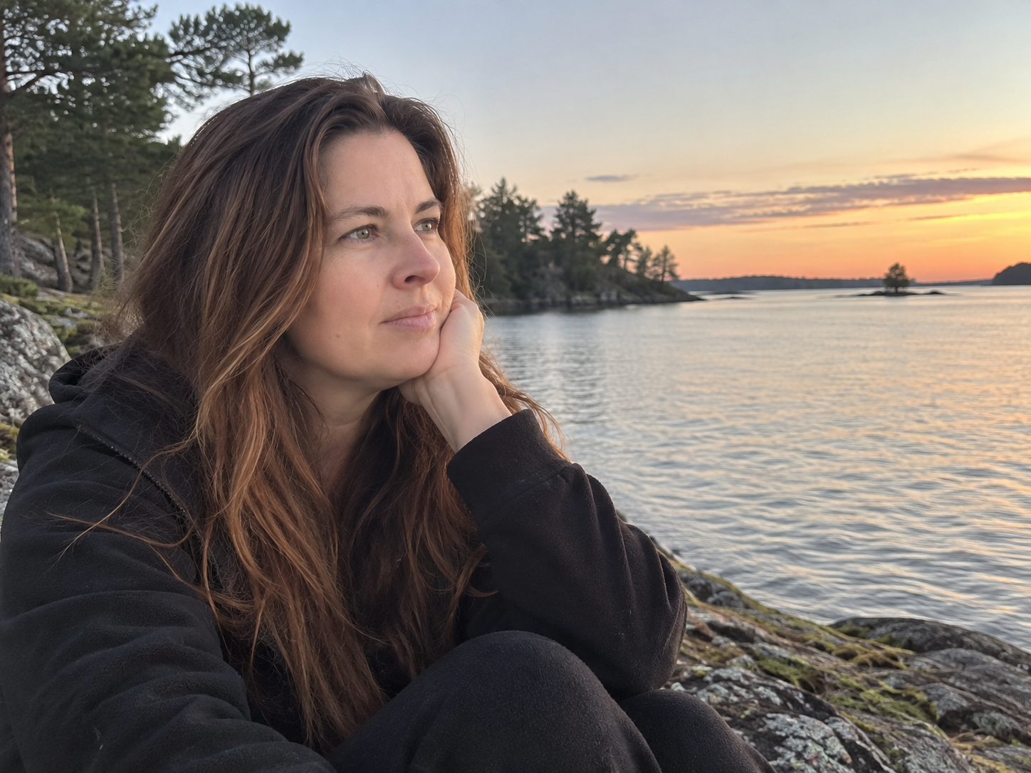 Kvinna sitter vid vattnet och blickar ut över sjön – en bild av att stanna upp och lyssna inåt.